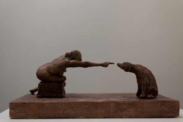 A ceramic sculpture by Michael Hermesh that depicts a seated woman leaning forward and pointing to the nose of a dog